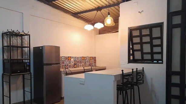 Eine kompakte Küche mit Kühlschrank, einer kleinen Kücheninsel mit Barhocker und einem Fenster mit Gittermuster.