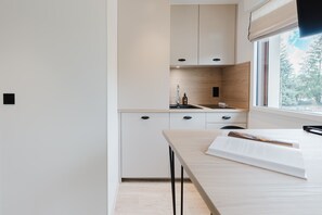 A modern kitchen with white cabinets, a wooden countertop, and a window with a view of trees. - 106 - Appart'Hôtel Neostelia-Annecy (Annecy)