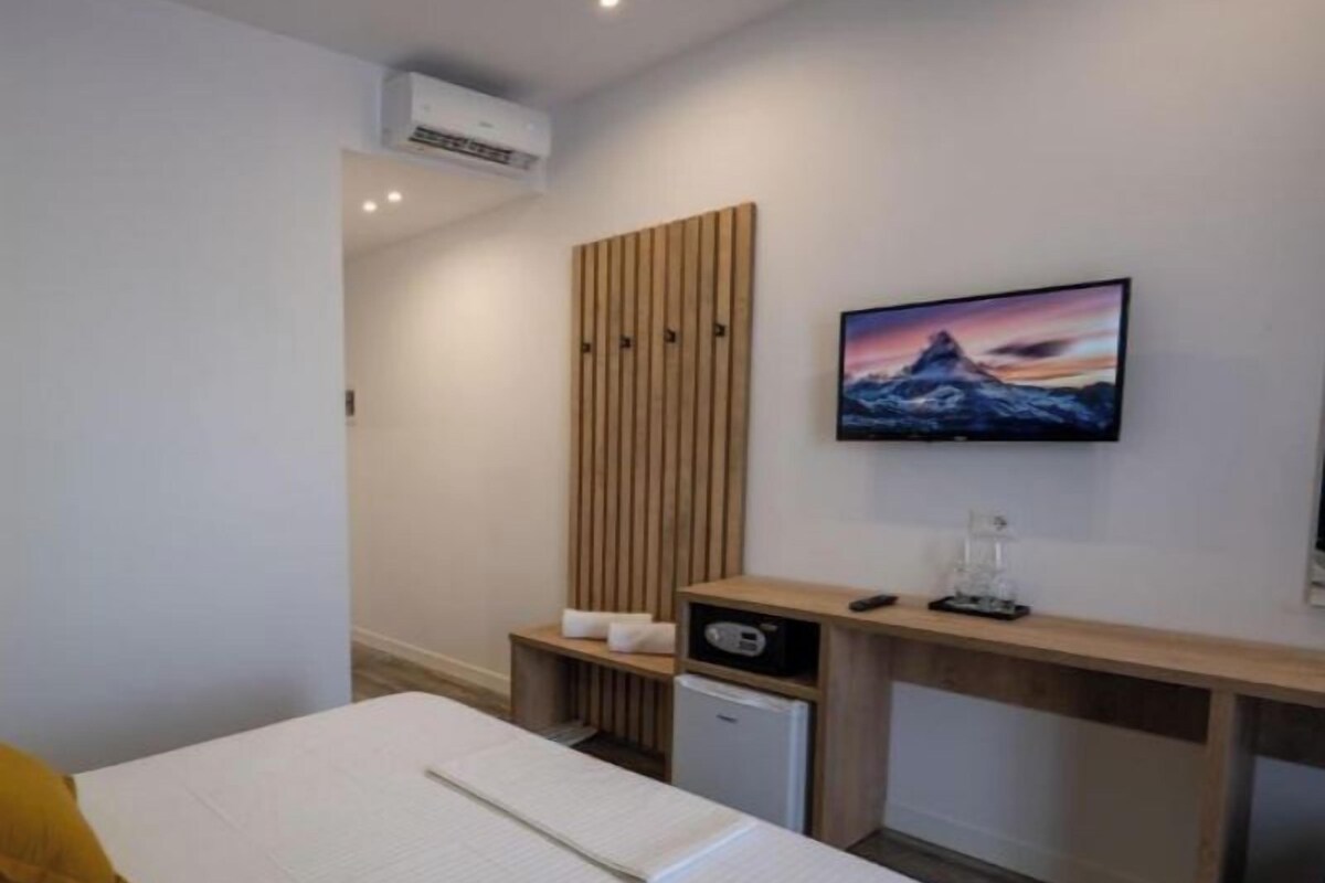 A hotel room with a bed, a desk, a television, and a wall-mounted air conditioner.
