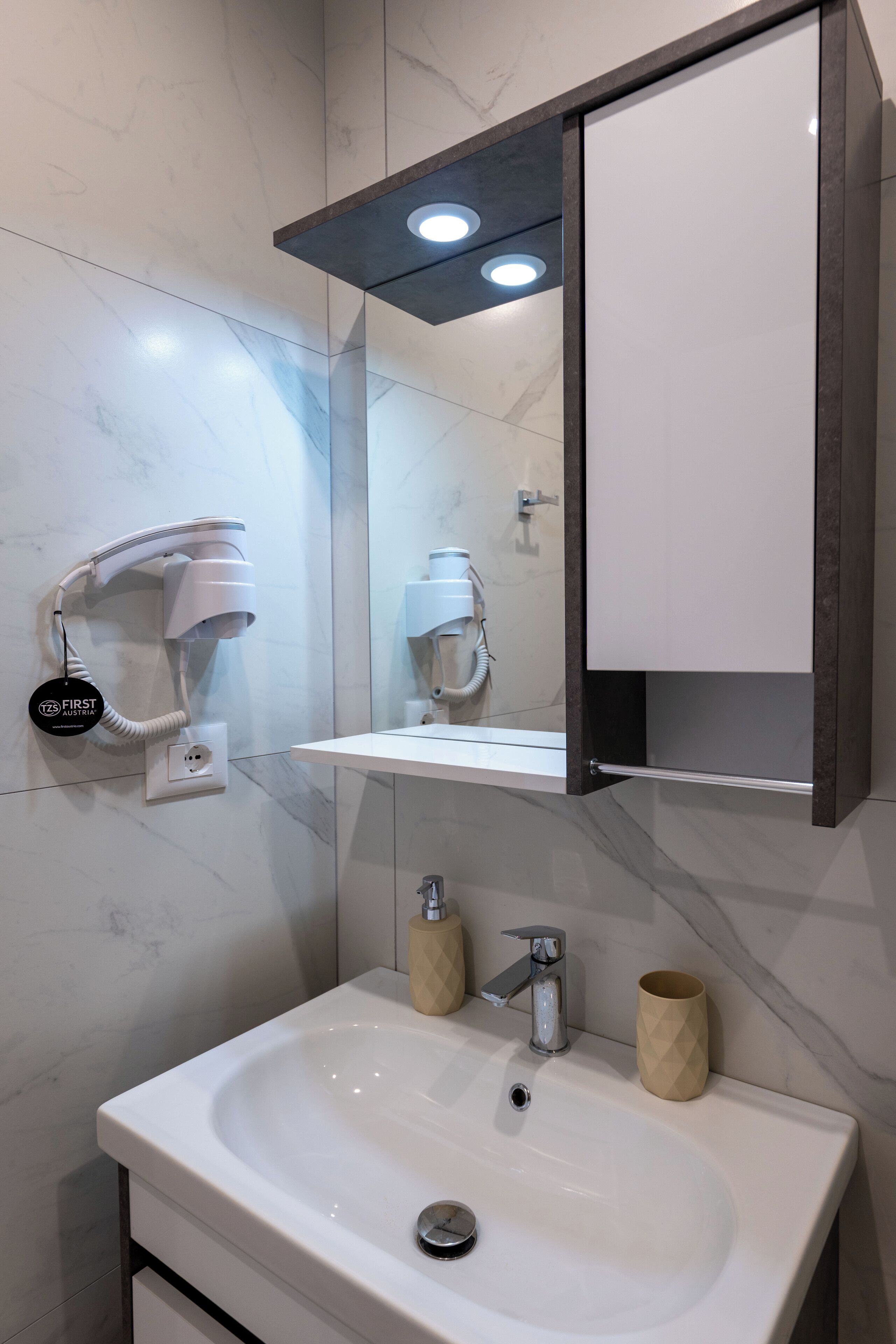 Un baño moderno con un lavabo blanco, un armario espejo y un secador de pelo montado en la pared.