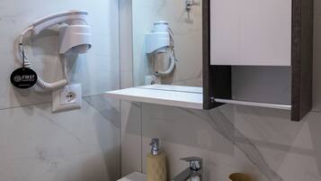 Un baño moderno con un lavabo blanco, un armario espejo y un secador de pelo montado en la pared.