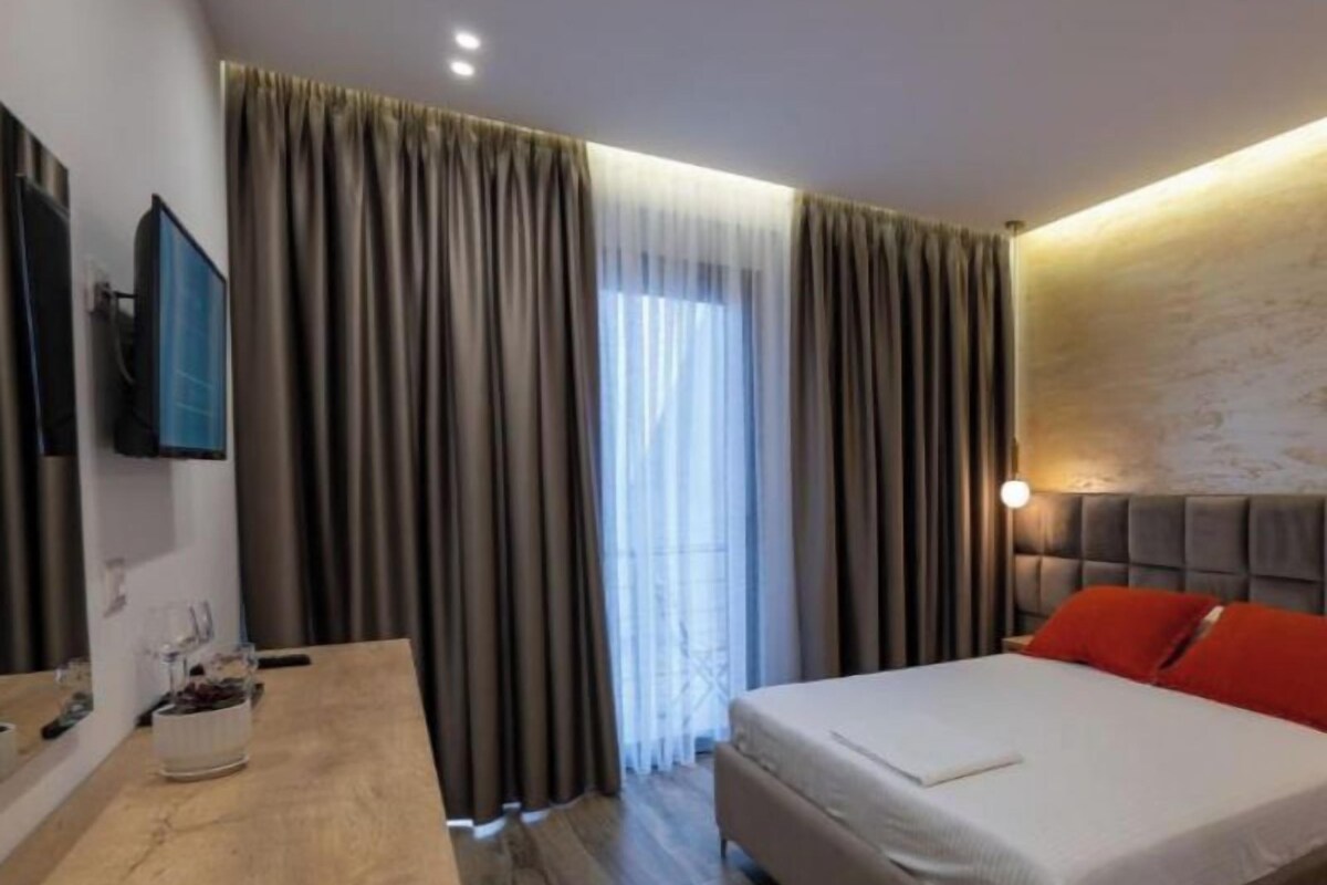 Una habitación de hotel moderna con un escritorio de madera, una cama grande con almohadas rojas y un televisor montado en la pared.