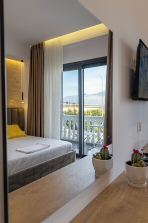 Una habitación de hotel moderna con cama, mesita de noche de madera, televisor montado en la pared y balcón con mobiliario exterior.