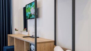A modern hotel room with a wooden desk, a television, a small refrigerator, and a bed with a blue headboard. - Hotel Flori (Sarandë)