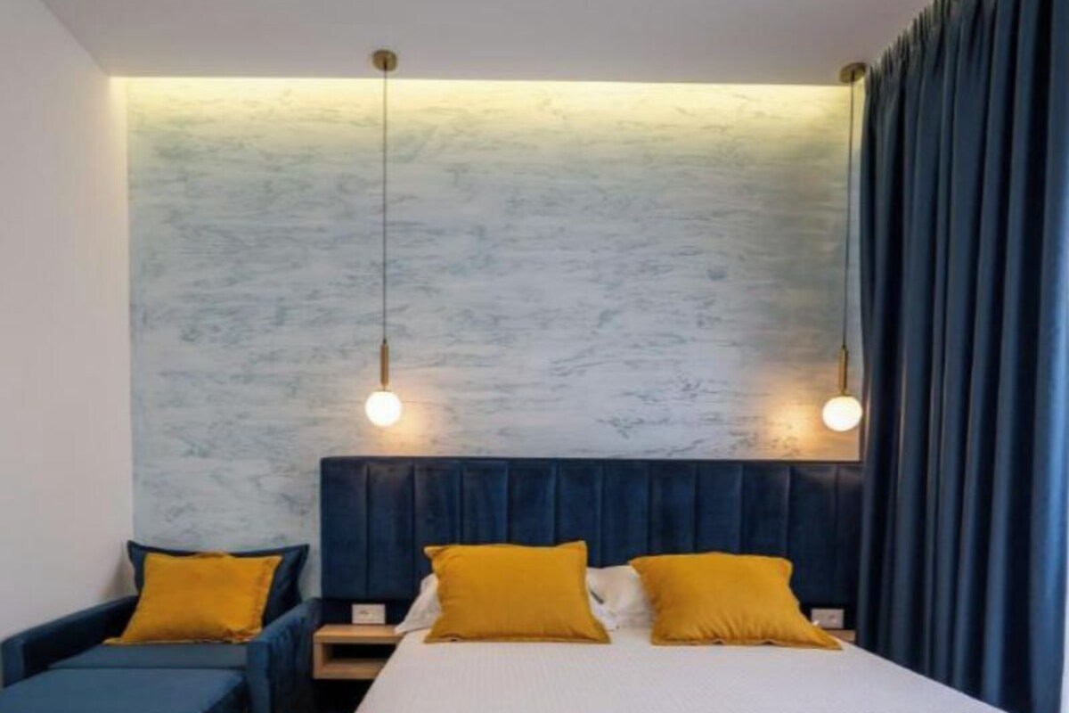 Habitación de hotel con cama, dos mesitas de noche, un sofá y una pared con textura.