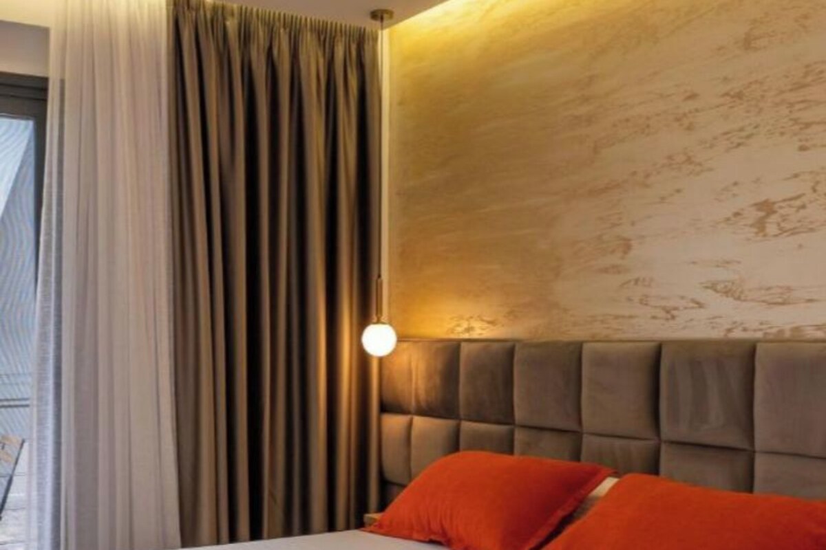 A hotel room with a bed, curtains, a wall-mounted light, and a textured wall.