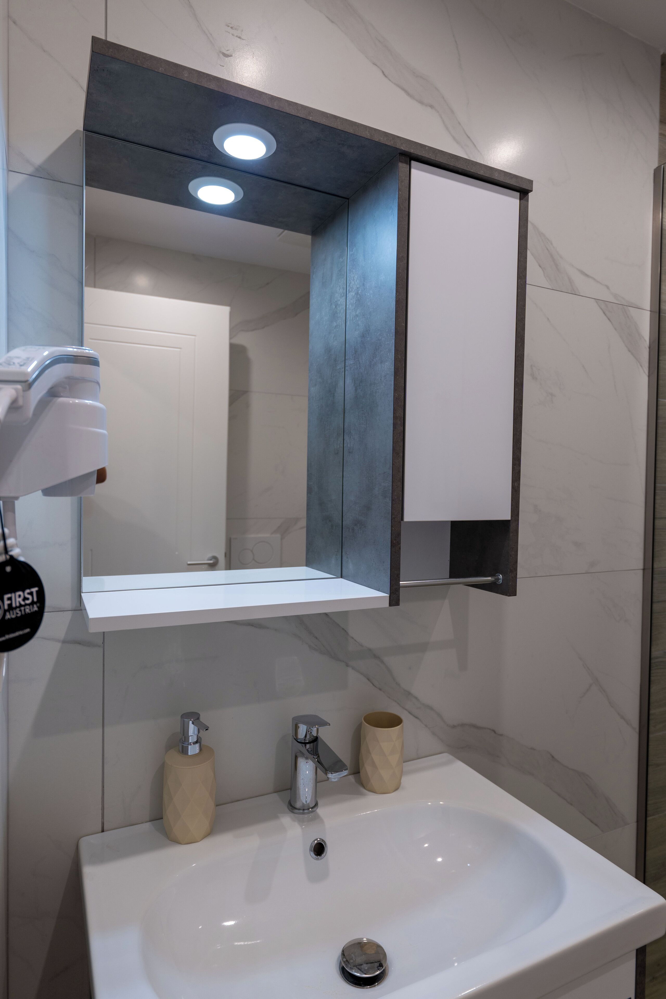 A bathroom with a white sink, a mirror, and a towel dispenser.
