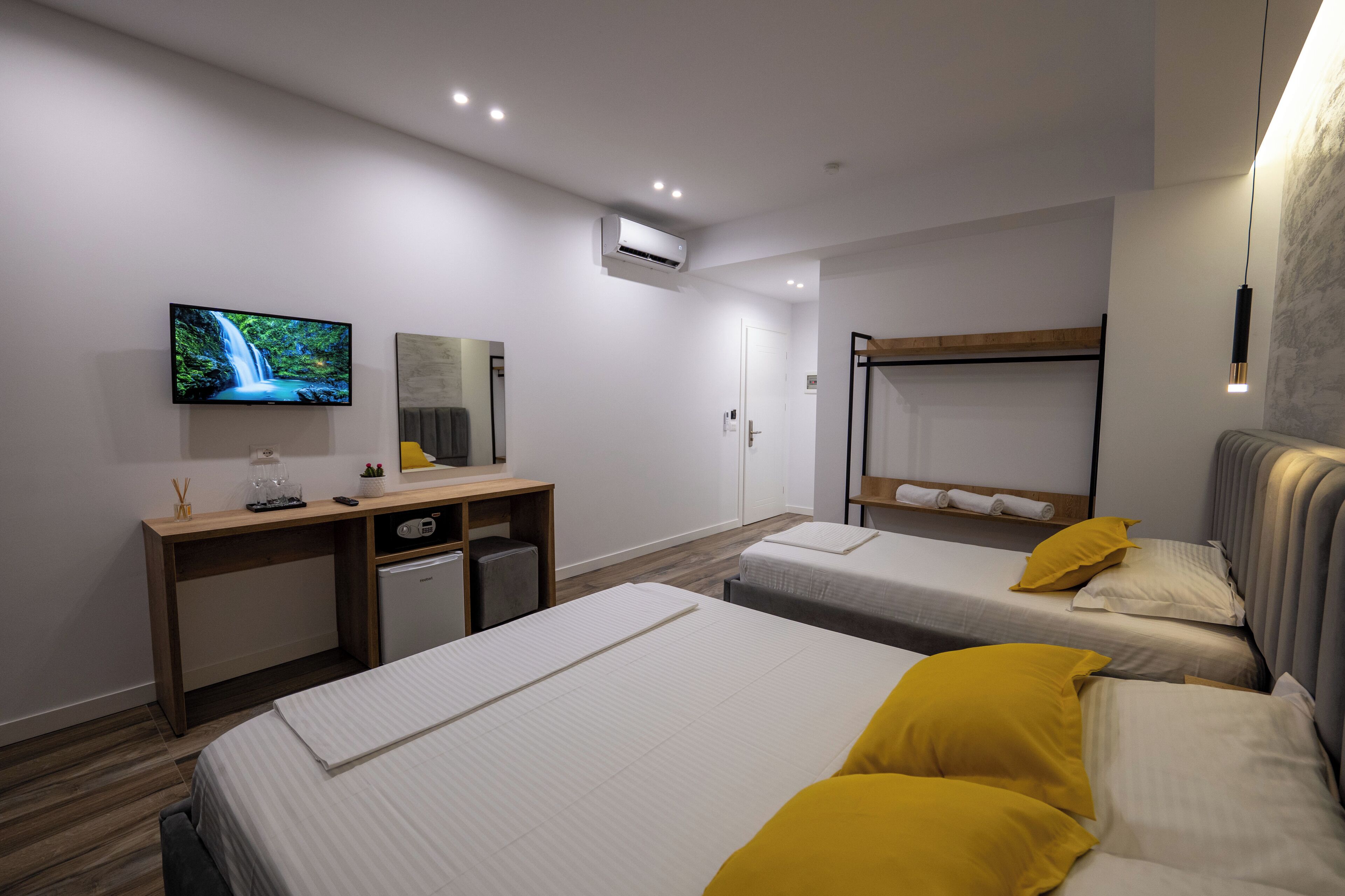 A hotel room with two beds, a desk, a TV, and a bunk bed.