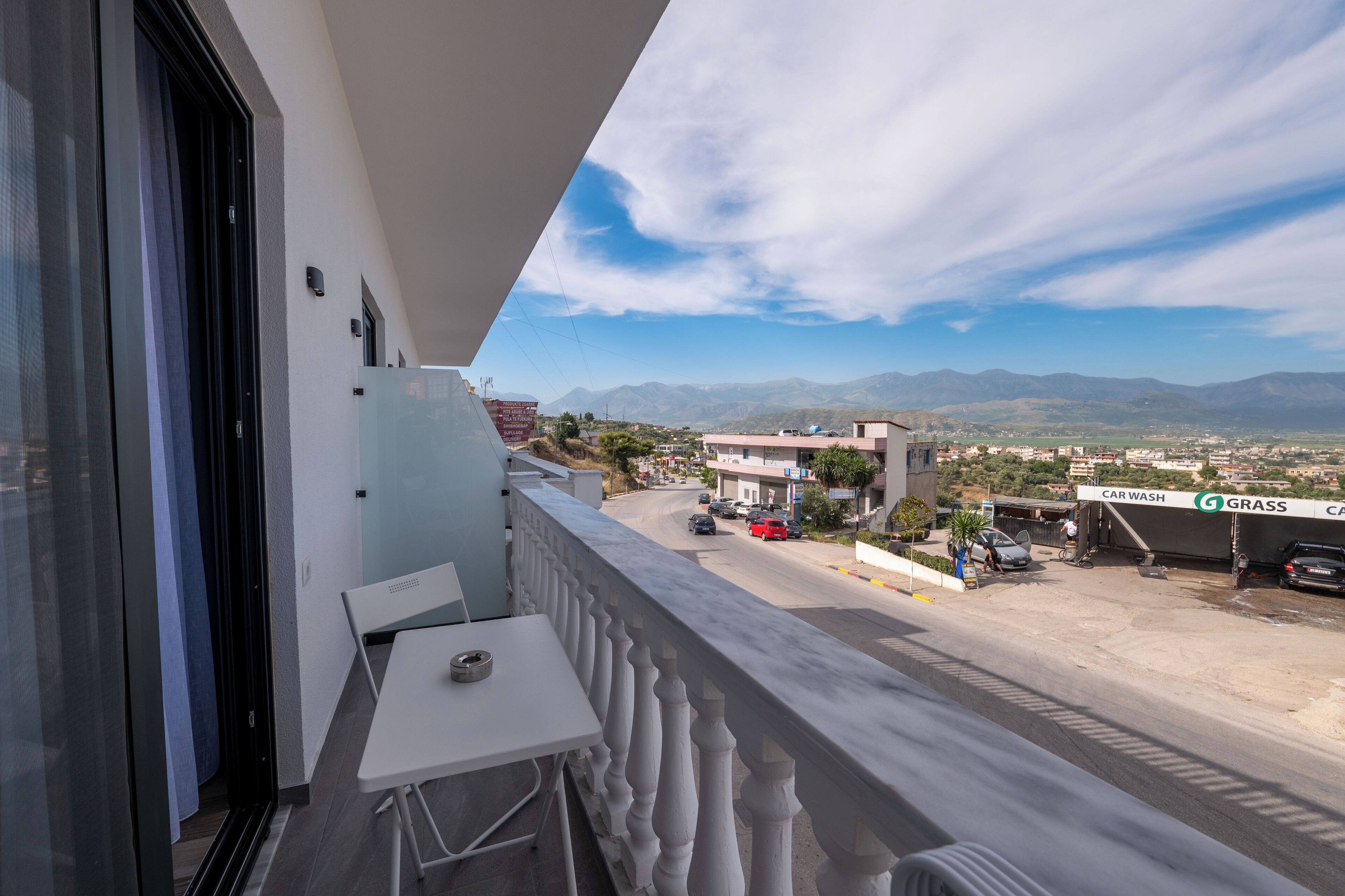 A balcony with a table and chairs, overlooking a street with cars and a car wash.