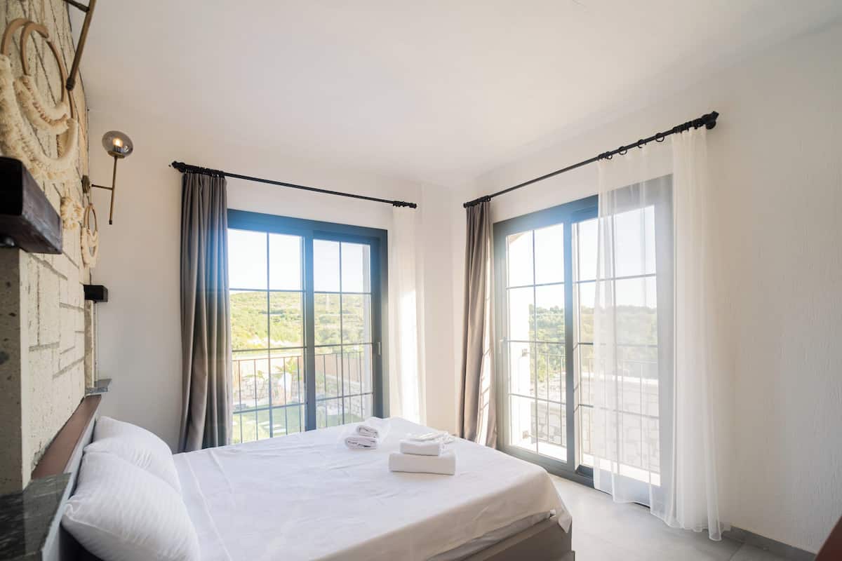 A bedroom with a bed, a window with curtains, and a view of the outdoors.