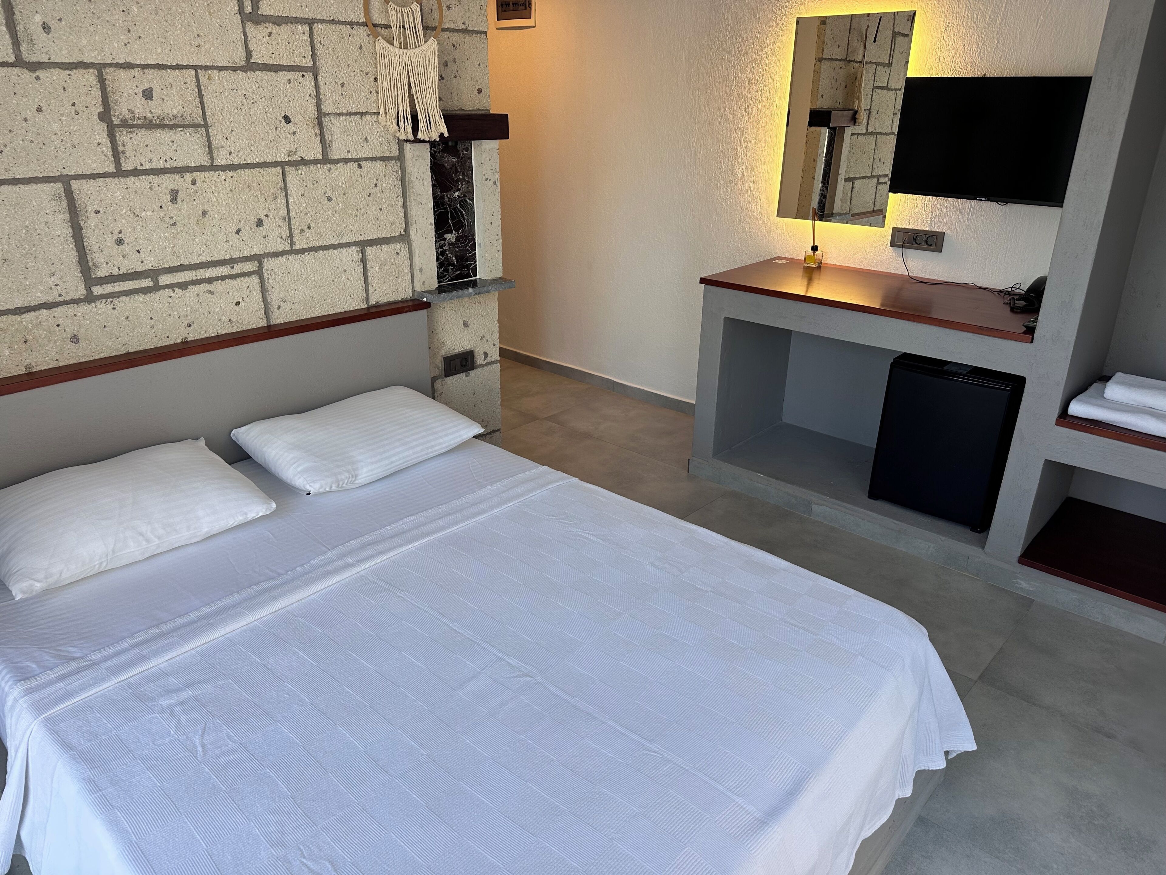 A hotel room with a bed, a small desk with a mirror, a TV, and a refrigerator.