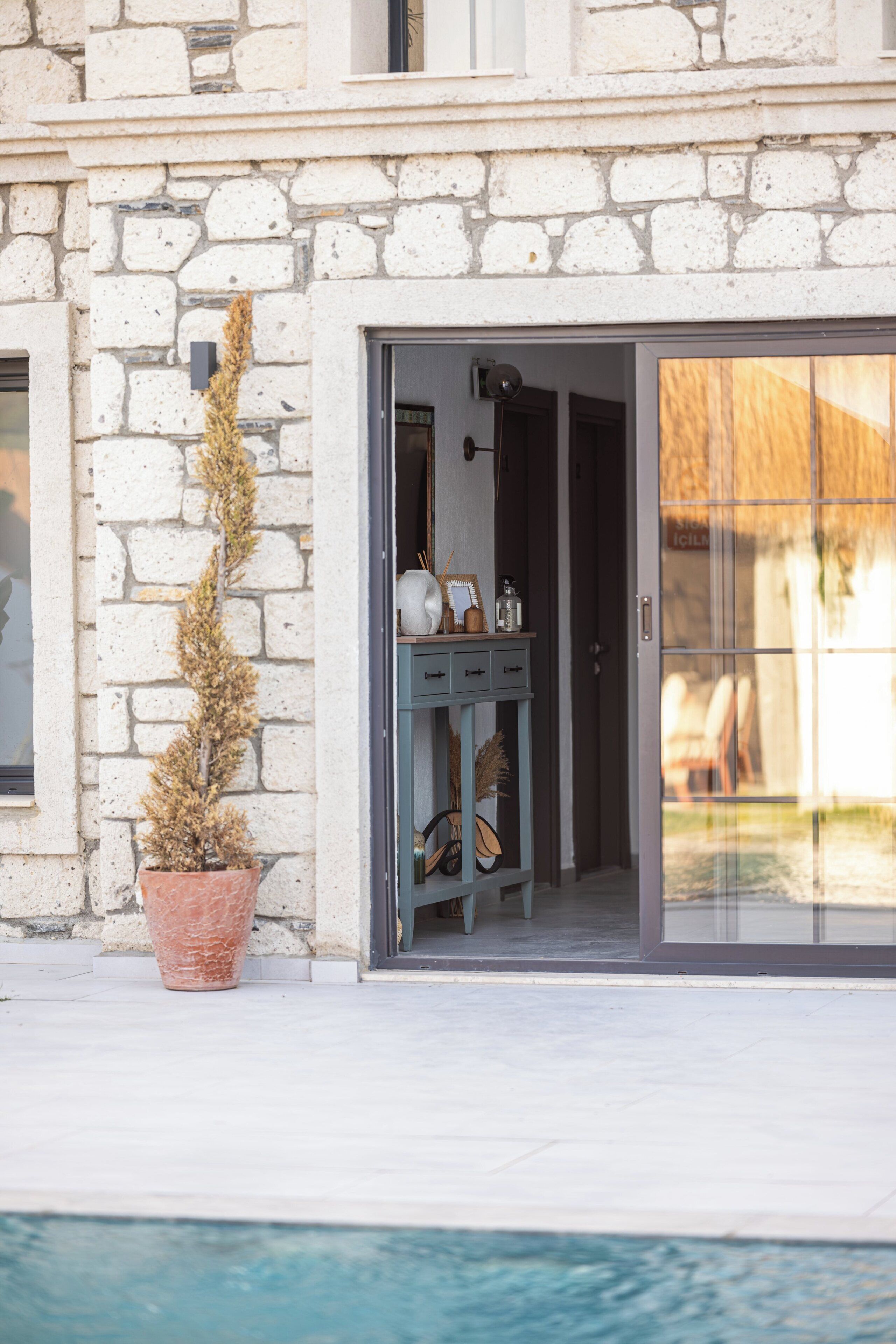 A stone building with a glass door leading to a room with a small cabinet and a potted plant.