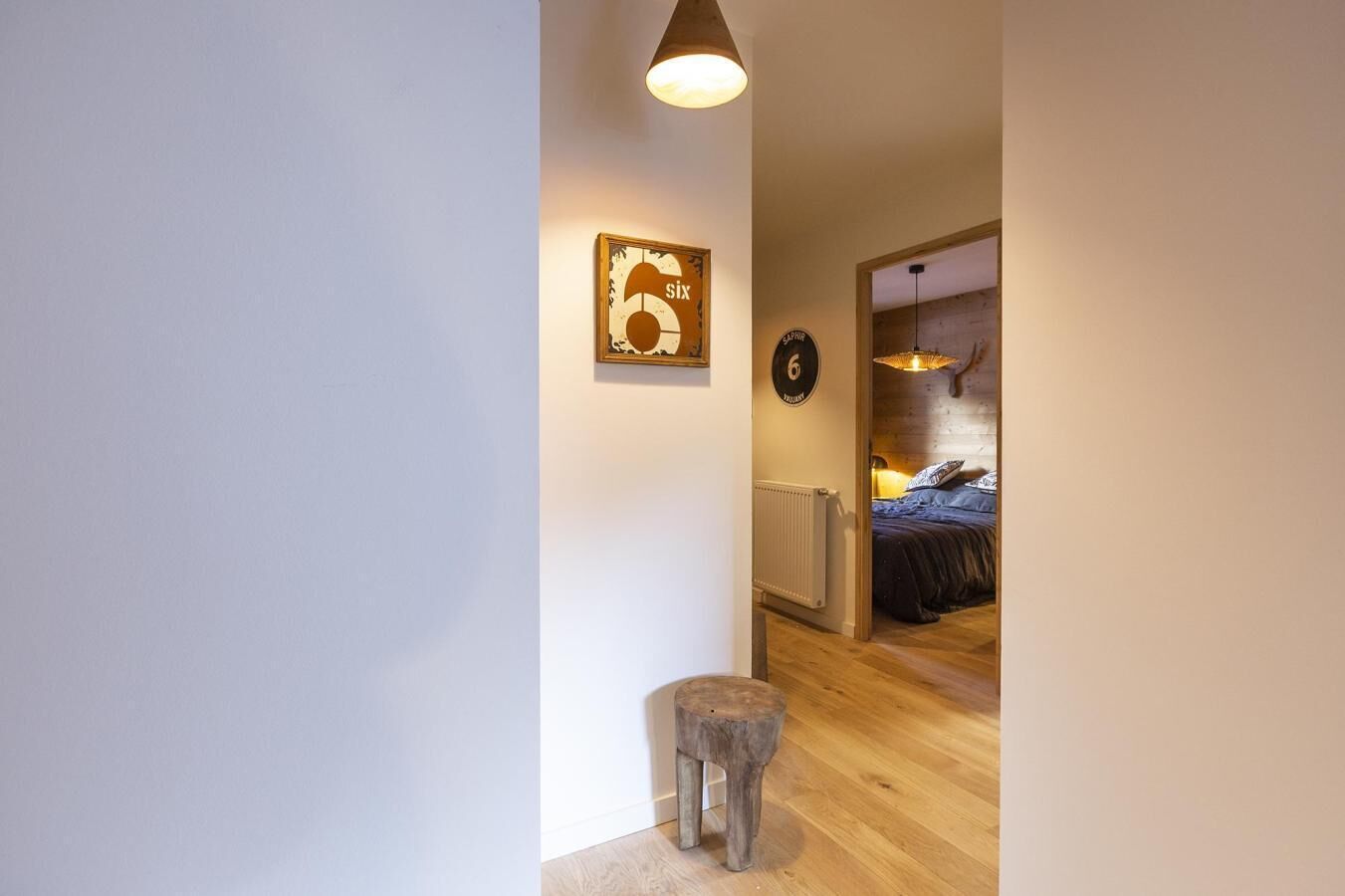 Ein Flur, der in ein Schlafzimmer führt, mit einem Bett, einem kleinen Hocker, einem an der Wand befestigten Schild und einer Deckenleuchte.