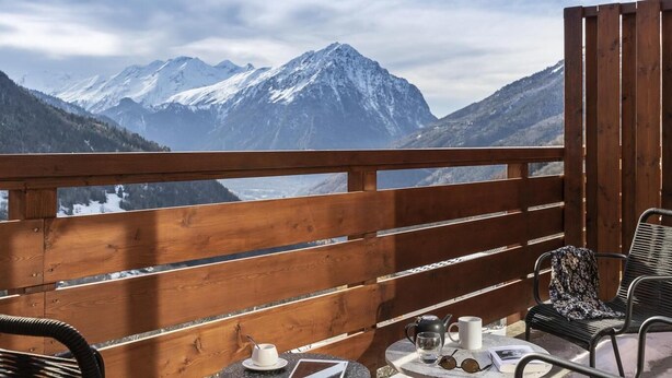 Ein Holzbalkon mit Tisch und Stühlen, mit Blick auf schneebedeckte Berge.