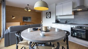 Eine moderne Küche mit weißen Schränken, einem eingebauten Backofen und einem Essbereich mit rundem Tisch und Stühlen.