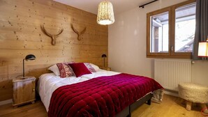 A bedroom with a wooden headboard, a large window, a red bedspread, and a woven pouf. - Wifi, 100m from resort center, balcony, parking, tv, ski locker, 55m², Vaujany (Vaujany)