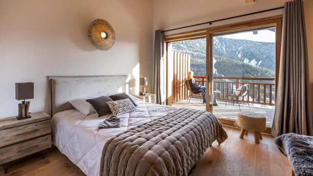 A bedroom with a large bed, a nightstand, a wall-mounted lamp, and a balcony with a view of mountains. - Wifi, 100m from resort center, balcony, parking, tv, ski locker, 55m², Vaujany (Vaujany)