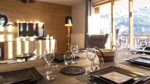 A dining area with a wooden table set for a meal, a television in the background, and a view of the outdoors through large windows. - Wifi, 100m from resort center, balcony, parking, tv, ski locker, 55m², Vaujany (Vaujany)