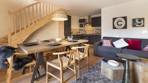 A modern living space with a wooden staircase, a dining area with a wooden table and chairs, a grey sofa with patterned cushions, and a kitchen in the background. - Wifi, 100m from resort center, balcony, parking, tv, ski locker, 55m², Vaujany (Vaujany)