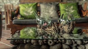 Een glazen salontafel met een rustiek middelpunt en twee glazen vazen met planten.