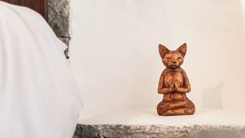 A small wooden statue of a cat sitting on a white shelf against a plain wall.