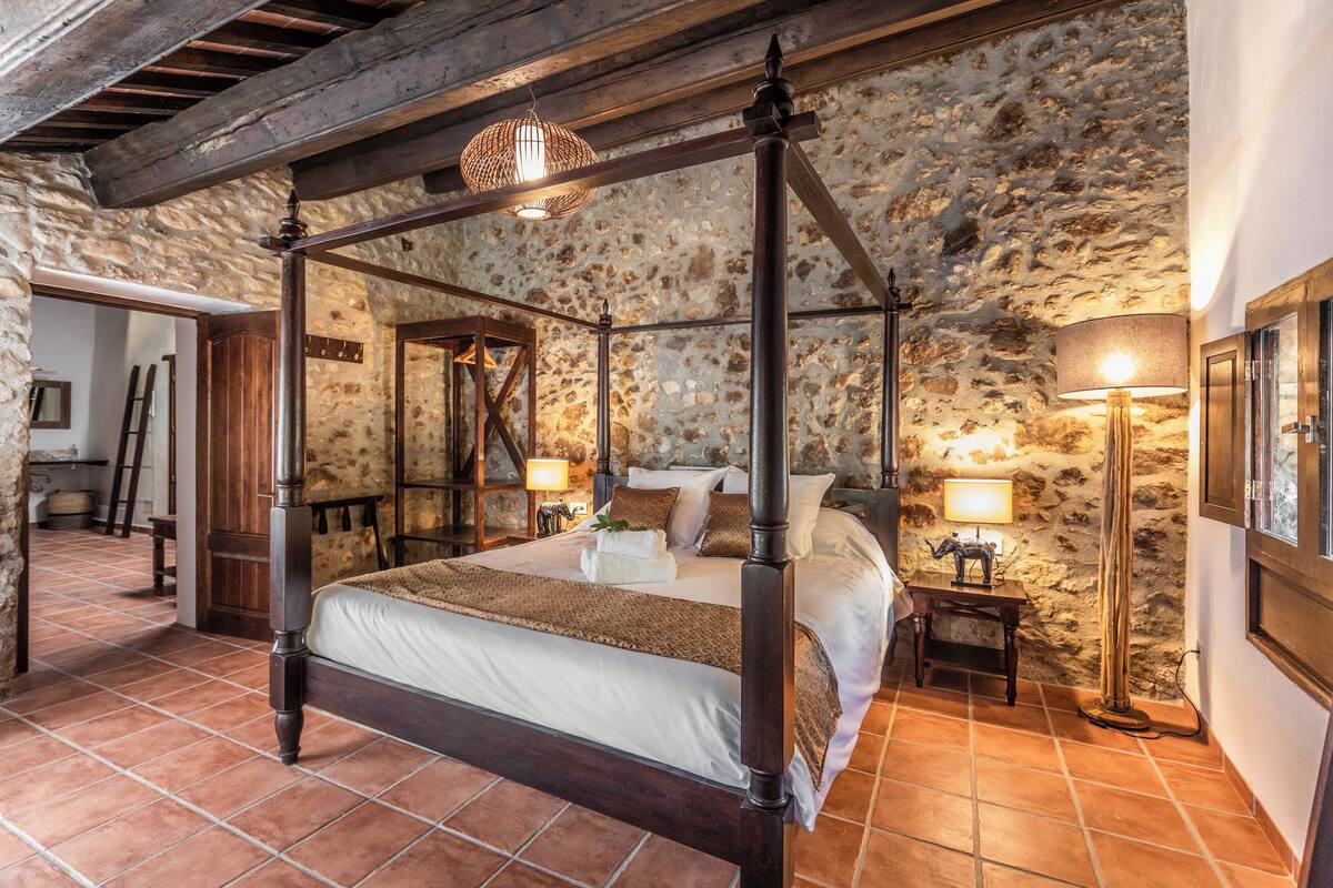 Un lit à baldaquin dans une chambre rustique aux murs de pierre et aux poutres apparentes.