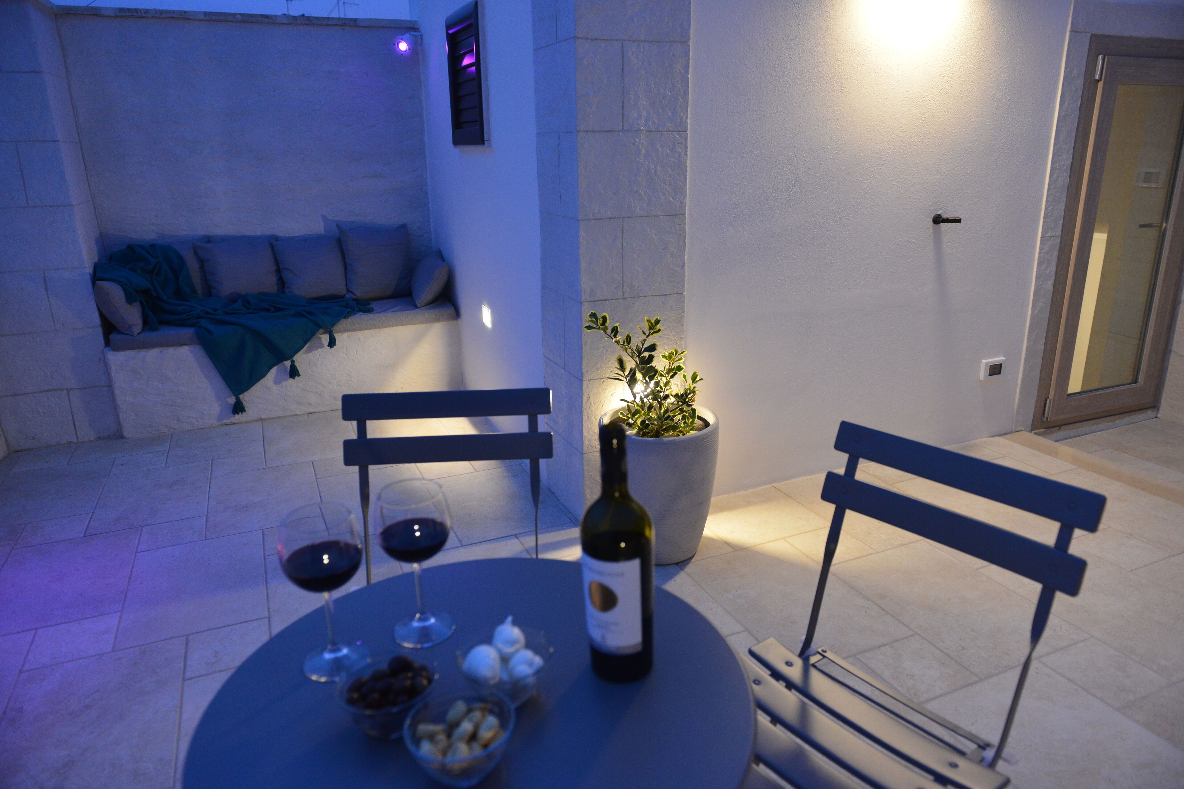 A cozy seating area with a sofa and a bench, a table with a bottle of wine and glasses, and a potted plant.