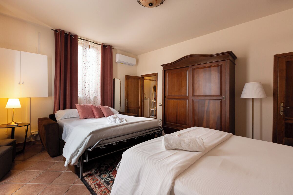 A hotel room with two beds, a wardrobe, a desk with a lamp, and an air conditioning unit.