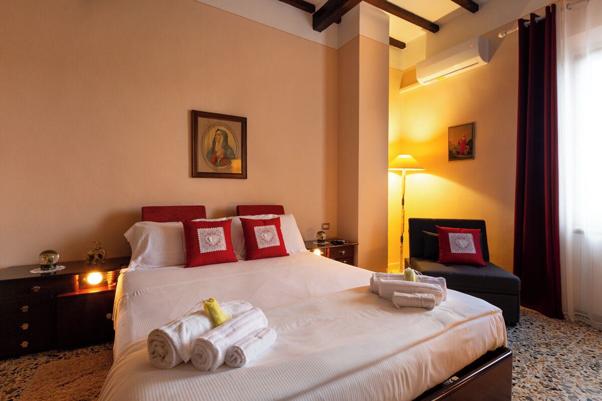 A neatly made bed with white and red bedding, a framed picture on the wall, and a bedside lamp.