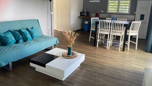 Un salon moderne avec un canapé de couleur turquoise, une table basse blanche et un coin repas avec des chaises blanches.