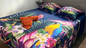 Una cama con colcha de motivos tropicales, un cabecero de madera y un ventilador de pared.