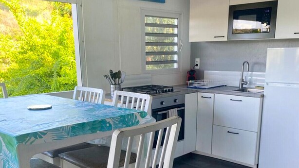 Una cocina moderna con armarios blancos, estufa a gas, lavamanos y ventana con vistas a la vegetación.