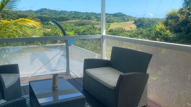 A covered outdoor seating area with wicker furniture and a view of a hilly landscape.