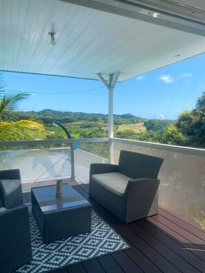 Un espacio de estar al aire libre con techo, mobiliario de mimbre y vistas a un paisaje montañoso.