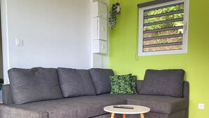 Ein modernes Wohnzimmer mit einem grauen Ecksofa, einem kleinen runden Tisch und einem Fenster mit horizontalen Rollläden.