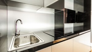Une cuisine moderne dotée d’un évier en acier inoxydable, d’un plan de travail noir et d’une plaque de cuisson intégrée.
