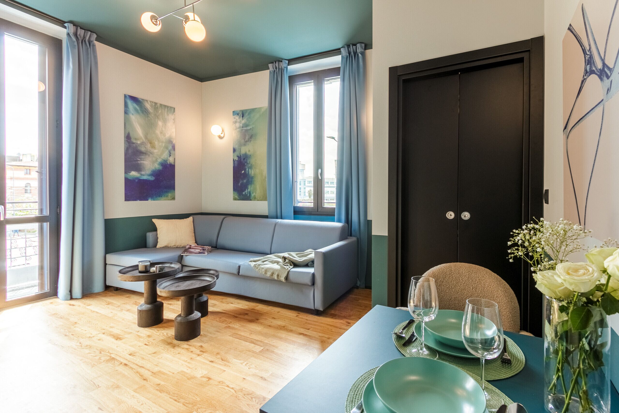 A modern living room with a grey sofa, wooden coffee table, and a dining area with teal tableware.