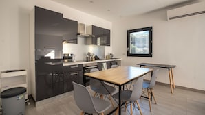 Una cocina moderna con comedor, que cuenta con una mesa de madera y sillas grises, un refrigerador negro y un ventanal que proporciona luz natural.