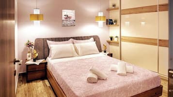 A neatly made bed with a pink bedspread, two bedside lamps, a nightstand with a vase of flowers, and a wooden wardrobe with a mirror.