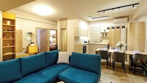A modern living room with a blue sofa, a small round coffee table, and a dining area with a wooden table and chairs.