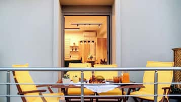 A balcony with yellow chairs and a table set for dining, overlooking a modern kitchen with wooden cabinets and a dining area.