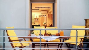 A balcony with yellow chairs and a table set for dining, overlooking a modern kitchen with wooden cabinets and a dining area.