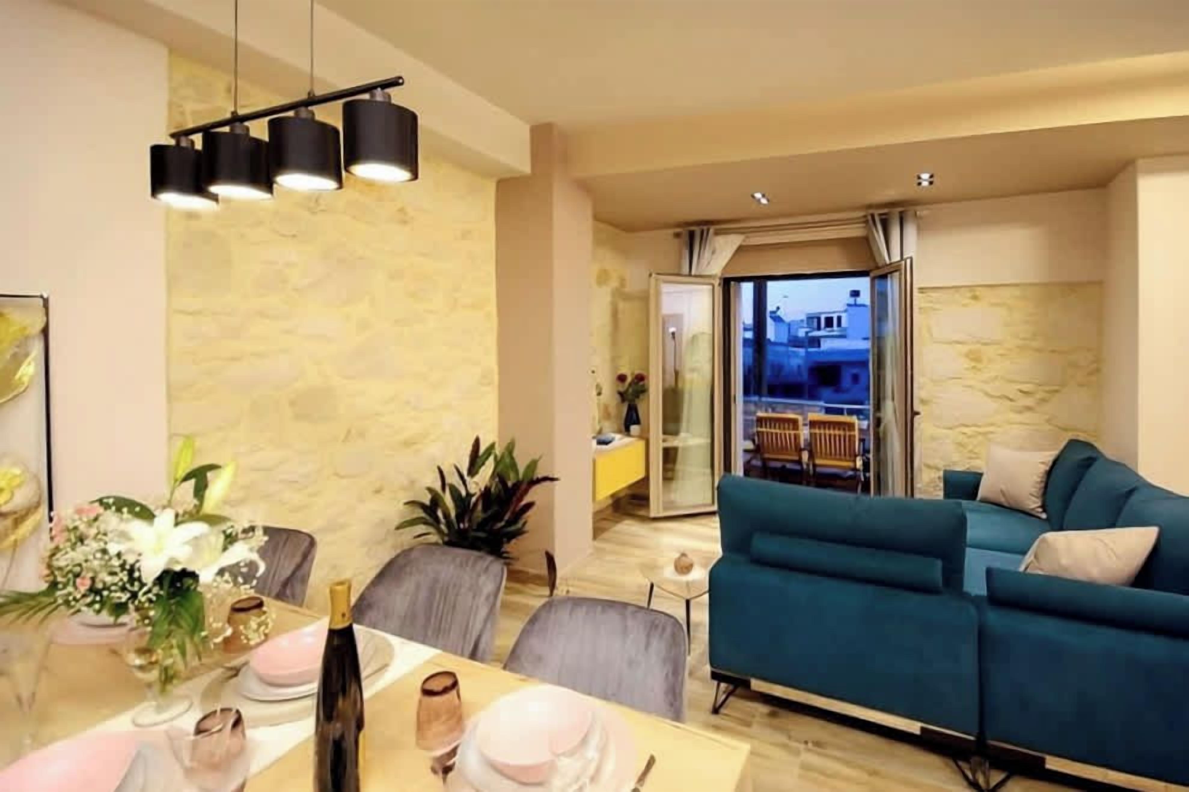 A modern living room with a teal sofa, a dining area with a glass table, and a stone wall.