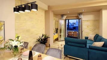 A modern living room with a teal sofa, a dining area with a glass table, and a stone wall.