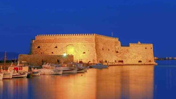 A large stone fortress with a moat, surrounded by calm water and boats.