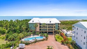 Een meerhoog hotel met een zwembad, omringd door weelderige begroeiing en uitzicht op de oceaan.