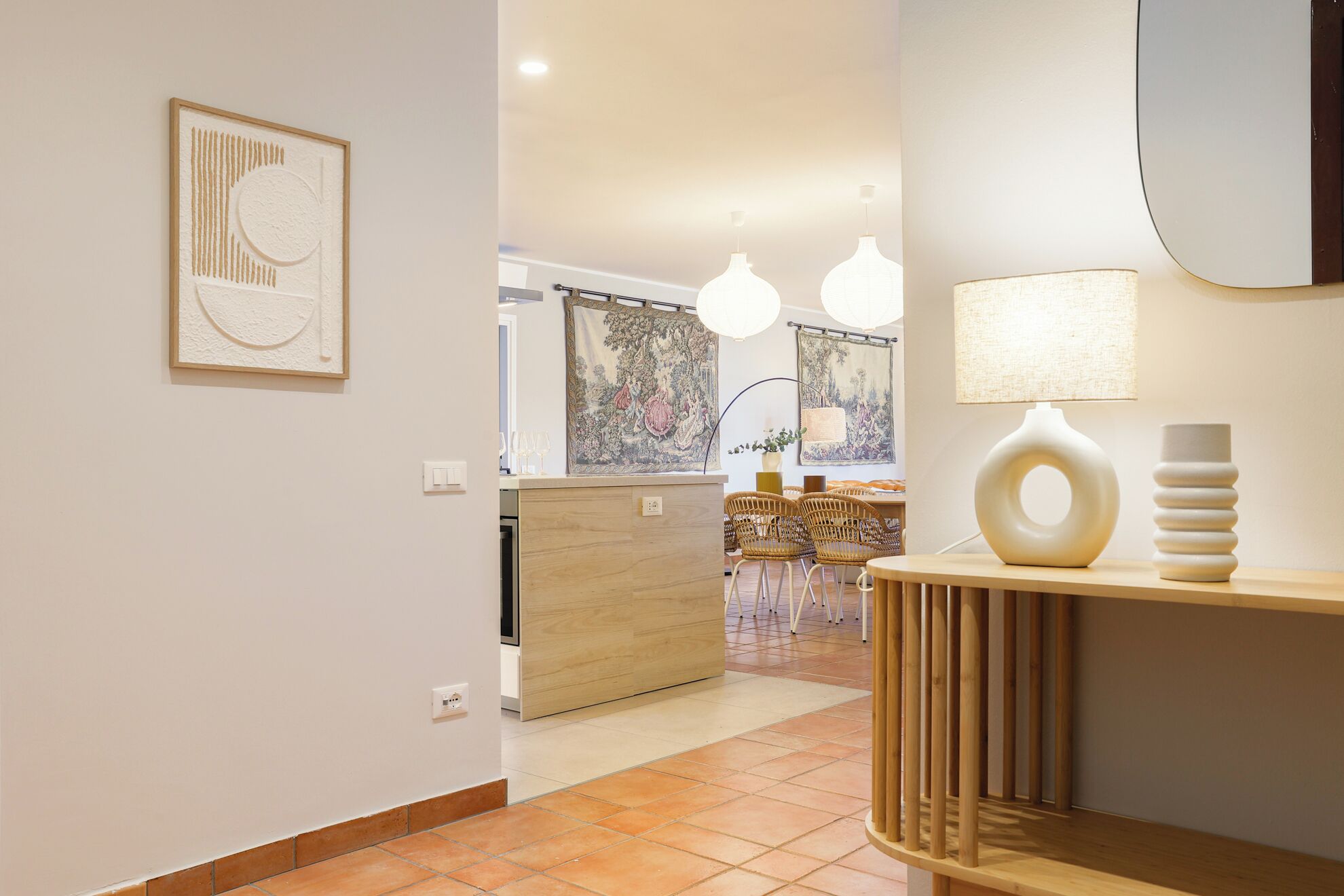A modern kitchen with a wooden countertop, two pendant lights, and a dining area with wicker chairs.