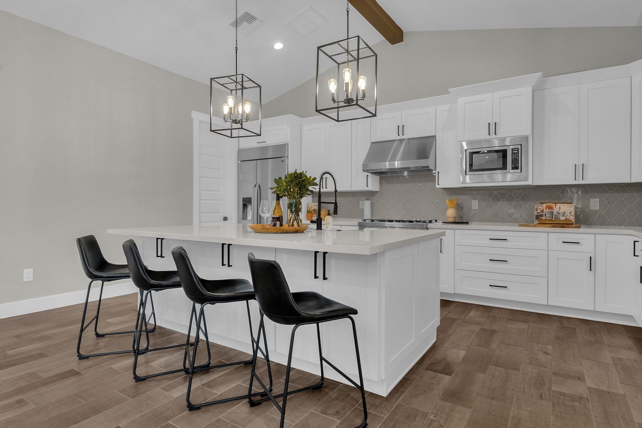 A modern kitchen with white cabinets, a central island with bar stools, stainless steel appliances, and pendant lighting.