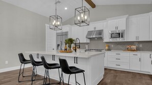 Una cocina moderna con armarios blancos, una isla central con taburetes de bar, electrodomésticos de acero inoxidable e iluminación colgante.