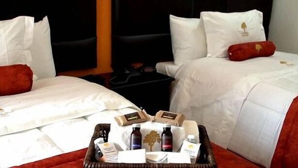 Camera d'albergo con due letti, ognuno con biancheria bianca e cuscini decorativi rossi. C'è un vassoio con articoli da toilette e una card sul letto davanti al letto a sinistra.